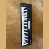 Černý MIDI kontrolér s klaviaturou. Na pravé straně je umístěno několik řad tlačítek, osm otočných potenciometrů a v horní části dva posuvníky. V pra…