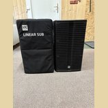 Na fotografii je černý subwoofer a přiléhající černý transportní kryt z látky. Na krytu je bílé logo „HK AUDIO“ a nápis „LINEAR SUB“. Subwoofer má če…