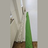 Na fotografii je stříbrný hliníkový mřížový truss v poloze vleže na podlaze. Vedle něj leží dlouhý zelený textilní kryt nebo přepravní vak. Na vybave…