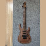 Elektrická kytara s přírodním dřevěným povrchem a hnědým hmatníkem. Nástroj má dva humbuckery, jeden kontrolní knoflík a přepínač zvukového výběru. N…