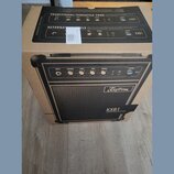 Kartonová krabice s fotografií černého basového komba. Na přístroji je viditelné logo Kustom a označení modelu KXB1. Horní část krabice obsahuje sché…