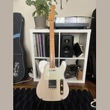 Elektrická kytara typu Telecaster v krémové barvě s bílým pickguardem a světle hnědým hnedem hmatníkem. Na hlavě je viditelné logo Squier. Nástroj st…