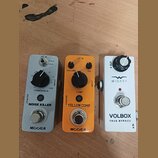 Tři efektové pedály v řadě na dřevěném povrchu. První je šedý s nápisy MOOER, NOISE KILLER a THRESHOLD. Prostřední je oranžový s nápisy MOOER, YELLOW…