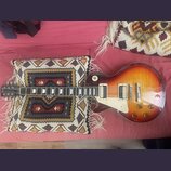 Elektrická kytara s trupem ve tvaru singlecut a barevným přechodem od žluté k tmavě hnědé (sunburst). Na hlavě je viditelné logo "Epiphone". Nástroj…