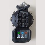 Černý digitální záznamový systém ZOOM H8 Handy Recorder. Zařízení má v horní části čtyři ovratové ovládací knoflíky s popisky MIC IN 1, 2, 3 a 4 a ná…