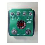 Zelený efektový pedál s nápisem ACOUSTIC EFFECTS PEDAL A2 a logem ZOOM v dolní části. Zařízení obsahuje několik otočných potenciometrů, červené kontr…
