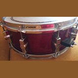 Fotografie znázorňuje snare drum s tmavě červeným dřevěným korpusem a chromovaným kováním. Na horním obruči je nápis SONOR 2.3mm PowerHoop doprovázen…