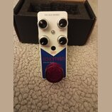 Bílý efekt pedál s červeným spínacím tlačítkem. Na horní části jsou čtyři černé ovládací knoflíky s popisky TIME, BLEND, MODULATION a FEEDBACK. Upros…