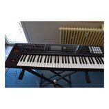 Černý digitální klavír značky Roland s označením RD-64. Na ovládacím panelu jsou nápisy D-BEAM, SOUND MODIFY a ARYTHMIA. Nástroj je umístěn na černém…
