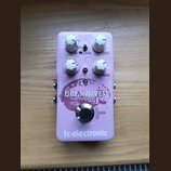 Světle fialový efekt pedál s nápisy BRAINWAVES PITCH SHIFTER a tc electronic. Na horní části jsou čtyři bílé otočné ovladače s popisky FX TYPE, VOICE…