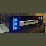Černý rackový distribuční panel s třemi modrými digitálními voltmetry a ampérmetry označenými L1, L2 a L3. Uprostřed je umístěn bílý proudový jistič…
