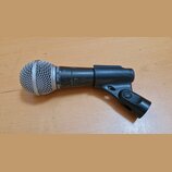 Černý dynamický mikrofon s kovovou stříbrnou mřížkou, umístěný v černém plastovém držáku. Na tětě mikrofonu je bílý nápis SHURE SM58 SHURE a na horní…