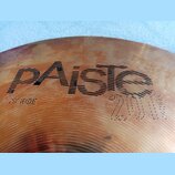 Detailní záběr na povrch činchy v bronzové barvě. Na povrchu je vidět nápis „paiste“ a pod ním označení „20" RIDE“. V pravé dolní části je vyryto „20…