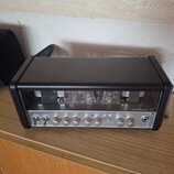 Černý kytarový zesilovač s kovovým předním panelem a průhledným krytem nad elektrony. Na průhledném krytu je bílý nápis „Hughes & Kettner“ a vpravo n…