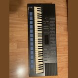 Černý digitální klavír s bílými a černými klávesami. V levém horním rohu je nápis YAMAHA a v levém dolním rohu nápis MUSIC-STATION. Nástroj obsahuje…