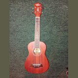 Hnědý dřevěný ukulele s nápisem „Oscar Schmidt“ na hlavě a svislým nápisem „Aloha“. U ozvukové otvory je umístěná barevná nálepka s motivem pláže. Ná…