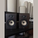 Dva studiové monitory v tmavě hnědém dřevěném provedení s rounded hranami. Každý reproduktor má v horní části výšek s černou mřížkou a ve spodní část…