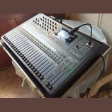 Digitální mixážní pult stříbrné barvy s velkým množstvím posuvníků, tlačítek a otočných ovladačů. Na pravé straně je vidět logo Soundcraft a název mo…