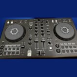 Černý DJ kontrolér s dvěma jog-koly a středovým mixážním sekcí. Na zařízení jsou viditelné nápisy DDJ-FLX4, rekordbox a serato, v dolní části je logo…
