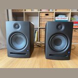 Dva černé studiové monitory v plastovém provedení. Na pravém dolním rohu každého reproduktoru je modrý čtvercový štítek s bílým nápisem JBL. Povrch j…
