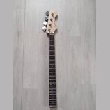 Fotografie zachycuje hmatník a hlavu basové kytary z přírodního dřeva s tmavým hmatníkem. Na hlavě je vidět nápis Squier JAZZ BASS a čtyři kovové lad…