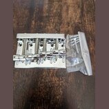 Stříbrný kovový kobylník na elektrickou kytaru s pěti sedly a odpružineným mechanismem. Na horní hraně je vyryt nápis GOTOH JAPAN. Vedle nástroje se…