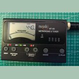 Černý digitální metronom a ladička s LCD displejem. Na přístroji je bílý nápis musedo MT-80 METRONOME & TUNER a označení MIC. Displej zobrazuje hodno…