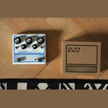 Bílý efekt pedál s nápisy DOD a RUBBERNECK ANALOG DELAY. Obsahuje tři černé ovládací knoflíky s popisky TIME, REPEATS a LEVEL, dva přepínače a několi…