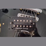 Černý humbucker s dvěma řadami snímacích pólů, umístěný v černém plastovém rámečku na černé kytare. Na spodní části snímače je bílý nápis Seymour Dun…