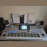 Stříbrný digitální klavír s nápisem YAMAHA a označením Tyros 4. Nástroj má v centru barevný displej, zahlreiche ovládací tlačítka a modře podsvícené…