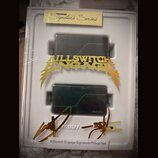 Dva černé humbuckery v bílém plastovém obalu, který je zabalen v průhledné fólii. Na horním okrape obalu je žlutý štítek s nápisem FISHMAN Signature…