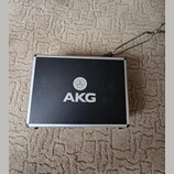 Černý obdélníkový kufr s hliníkovým rámem. Uprostřed víka je bílé logo a nápis AKG. Povrch kufrů vykazuje mírné znečištění a drobné oděrky. V pravém…
