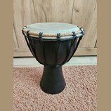 Černý djembe s hrací plochou z pleti v přirozené světlé barvě. Horní okraj je opleten kombinací černého a béžového provázku. Na těle nástroje nejsou…