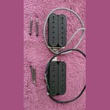Dvě černé humbucker snímače s kovovými základnami a připojenými kabely v šedé a černé barvě. Vedle snímačů jsou položeny čtyři montážní pružiny s šro…