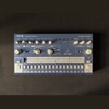 Modré analogové bicí automaty s bílými popisky a ovládacími prvky. Na přístroji jsou nápisy RD-6 Computer Controlled Analog Drum Machine a logo behri…