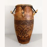 Dřevěný buben s hnědým povrchem a koženou membránou, která je upevněna černými provazy. Tělo nástroje obsahuje vyřezávané ornamenty ve formě vlnitých…