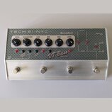 Stříbrný kytarový pedál s texturovaným šedým předním panelem a čtyřmi stoupacími spínači. Na panelu je červeně napsáno "VT Bass DELUXE" a v dolní čás…