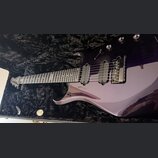 Fialová elektrická kytara v černém polstrovaném kufru. Na hmatníku je viditelný nápis "Custom Shop". Kytara má dva snímače typu humbucker a fixní mos…