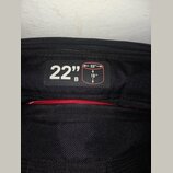 Detail černé texturované látky s přišitou černou štítkem. Na štítku je bílý nápis 22" B a schéma obdélníku s rozměry 22" a 18". Pod štítkem je vidite…