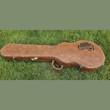 Hnědý tvrdý kufýr na kytaru s kovými zapínacími zámky a úchytem. Na pravé straně je vidět černé logo s nápisy USA a Gibson. Povrch vykazuje známky op…