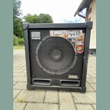 Černý basový kombozesilovač s kovovou ochrannou mřížkou přes reproduktor. Na přední straně jsou viditelná loga a nápisy: "Roland", "CUBE-120XL BASS",…