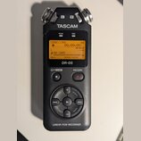 Černý digitální záznamový zařízení s nápisy TASCAM a DR-05. Displej zobrazuje hlášku NO CARD a časovač 00H00M00S. V dolní části je nápis LINEAR PCM R…