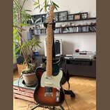Elektrická kytara s tmelelovým povrchem v přechodu od černé k hnědé a žluté barvě. Na hlavě je viditelné logo Fender. Kytara má bílý pickguard, jeden…