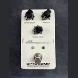 Bílý efekt pedál s třemi černými otočnými knoflíky, označenými jako Compression, Release a Output Level. Na spodní části je nápis OPTO COMP a Analog…