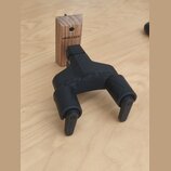 Černý plastový držák na hudební nástroj s dvěma rameny. Na horní části a na spodních páčkách je vyražen nápis HERCULES. Vedle držáku je dřevěný blok…
