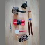Sestava různých perkusních nástrojů na světlé podlaze. Soubor obsahuje černý buben s kovovými plátky, červené shakerové trubice, dřevěný guiro s modr…