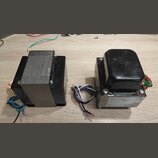 Dvě elektrické transformátory s kovovými jádry a černým krytím. Levý kus má část jádra odkrytou, pravý je z horní strany zakryt černým plastovým nebo…