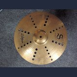 Zlatý kovový činel s otvory v povrchu. Na povrchu jsou nápisy Zildjian, TRASH CRASH a 16"/40 cm spolu s logem ve tvaru písmene S. V dolní části je dr…