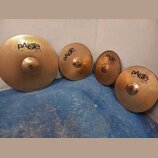 Čtyři mosazné činely značky Paiste v různých velikostech. Na činelech jsou čitelné nápisy „paiste 2002“ a konkrétní označení: „20" RIDE“, „16" CRASH“…