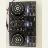 Černý DJ kontrolér s dvěma jog-koly a centrální sekcí s knoflíky a posuvníky. Na přístroji jsou viditelné nápisy Hercules, DJCONTROL IMPULSE 200 a DJ…